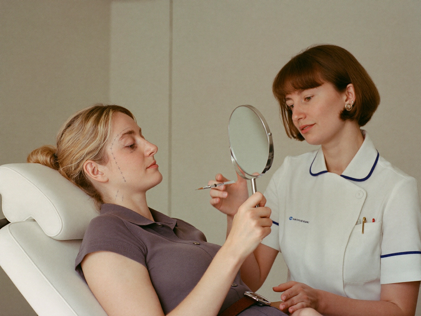 A nurse injector and a client looking together at a hand mirror during a consultation