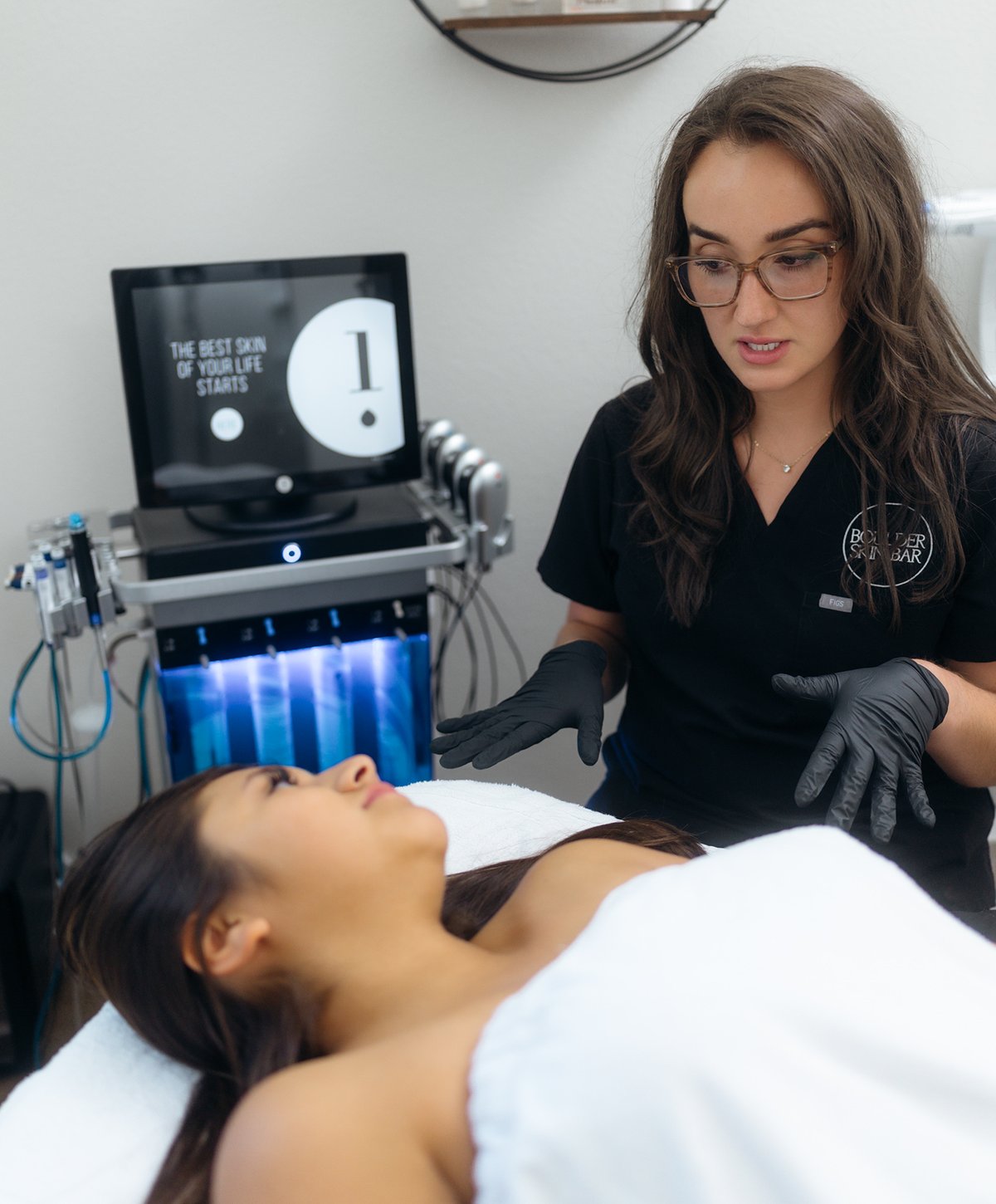 Esthetician with a client beside the HydraFacial system at Boulder Skin Bar