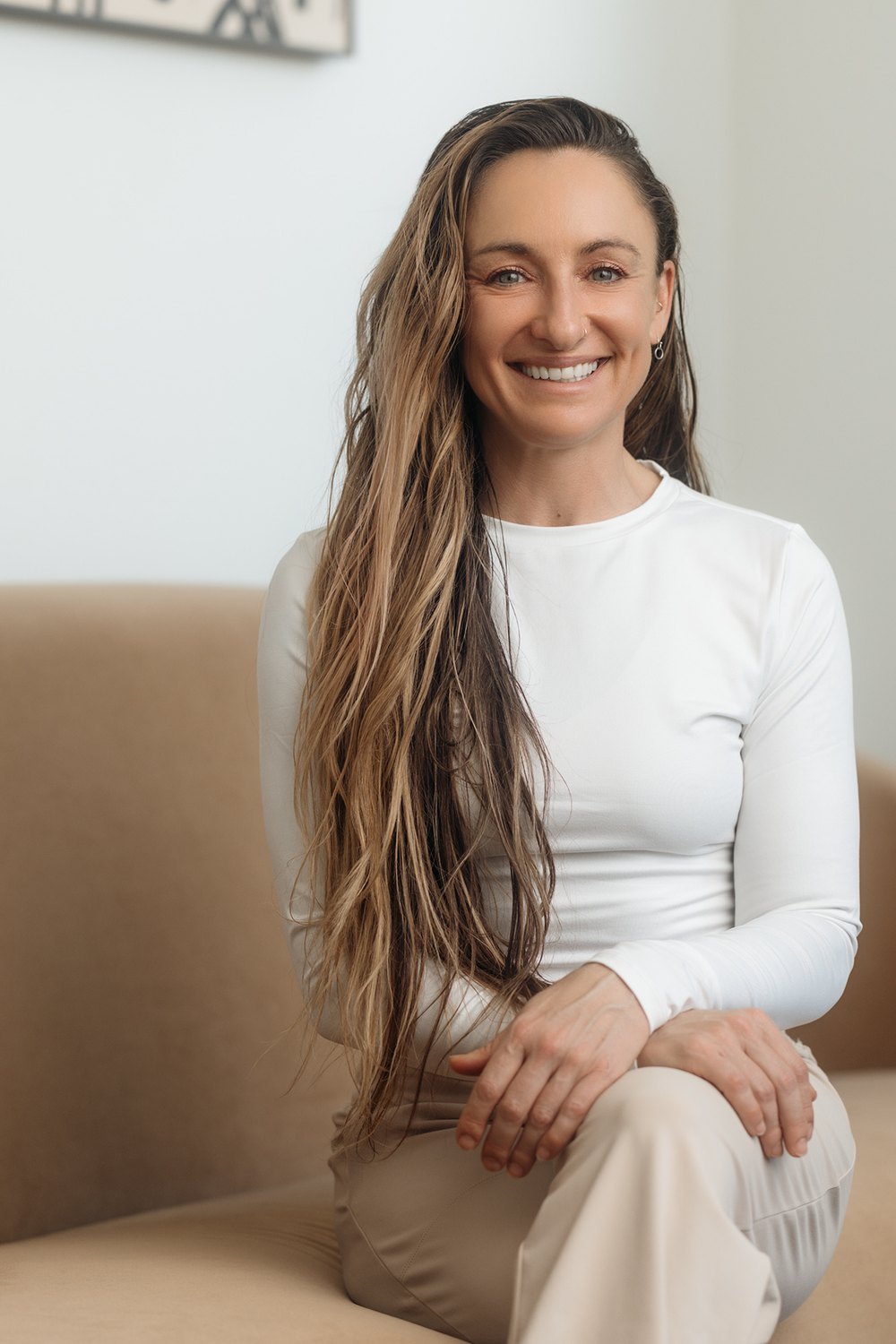 Smiling woman with long hair seated on a sofa.